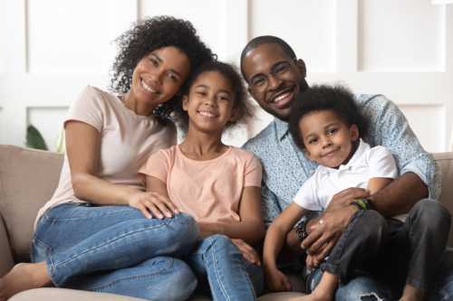 A family of a mom, dad, son and daughter sit on a couch smiling.