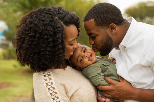 Black mom and dad and baby hugging together.