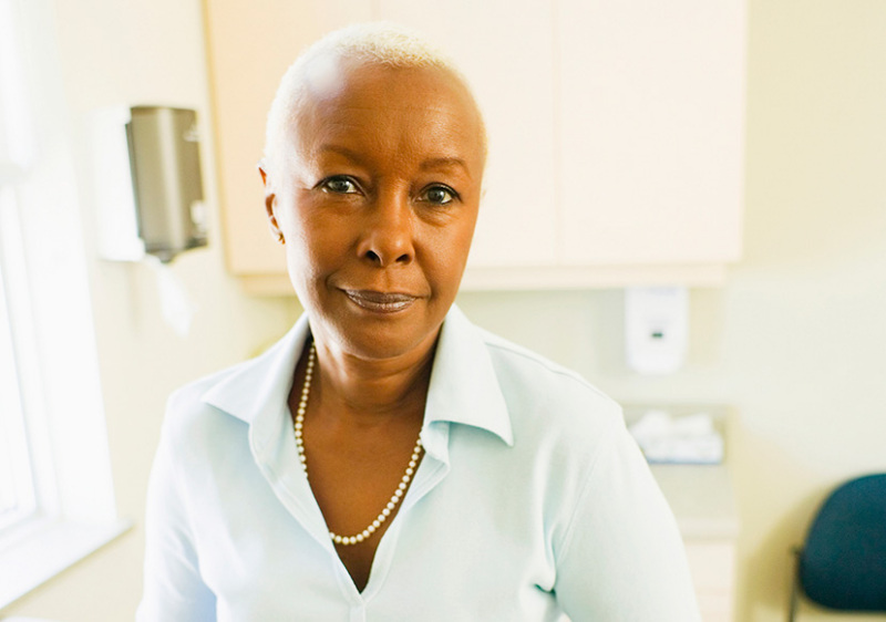 Portrait of a Black woman in her 50s or 60s sitting on an exam table.