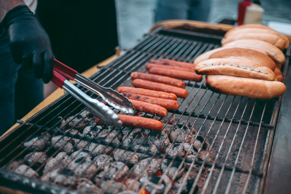 Person with gloves on grilling hot dogs.