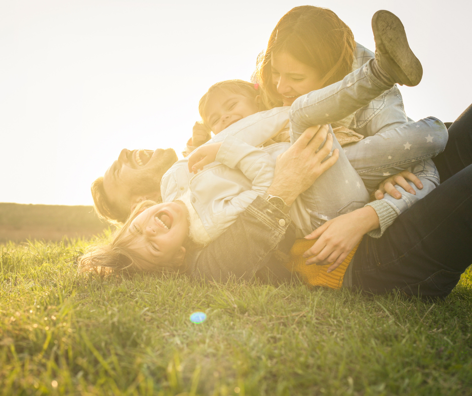 Family of four plays in the grass with sun in the background.