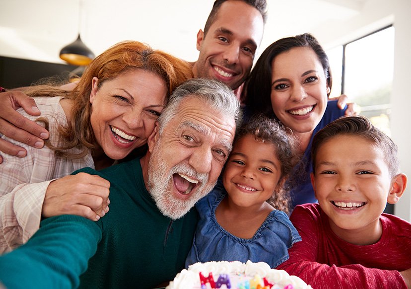 multi-generational family poses together for a selfie behind a birthday cake.