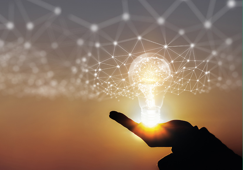 A concept of innovation and networking. A silhouette of a hand holding a bright lightbulb with a web of connections around it. There is a a sunrise in the background.