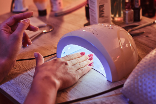 Woman curing her gel nails under an ultraviolet light at a nail salon.