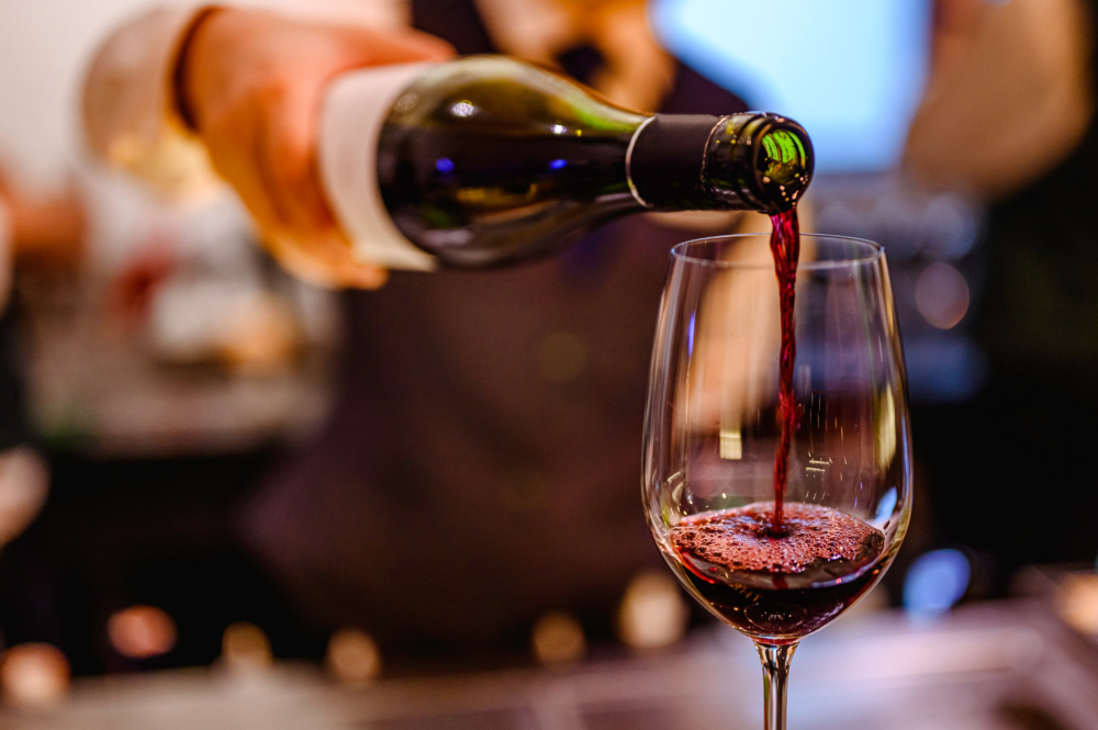 Bartender pouring red wine into a glass sitting on the bar.