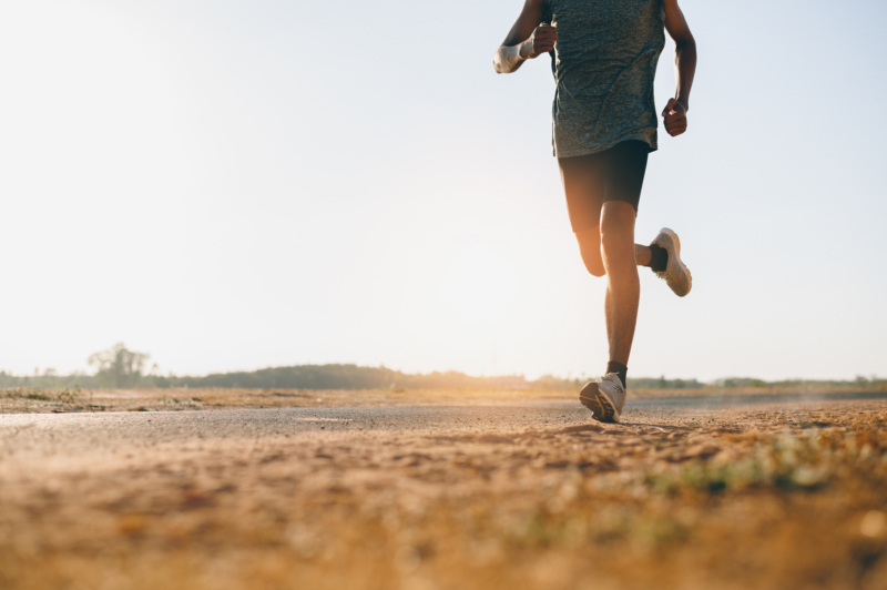 Athlete running along a flat road with sun in the background.