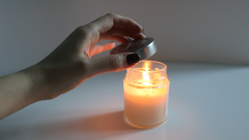 Womans hand covers a burning scented candle with lid, extinguishing the flame. The candle's light creates warm, cozy atmosphere. Idea for meditation, spa procedures, self care, setting romantic mood.
