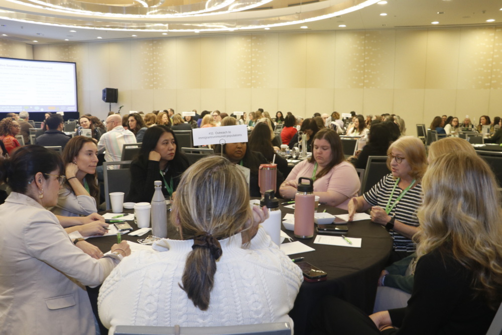 Groups of people sit at large, circular tables discussing topics.