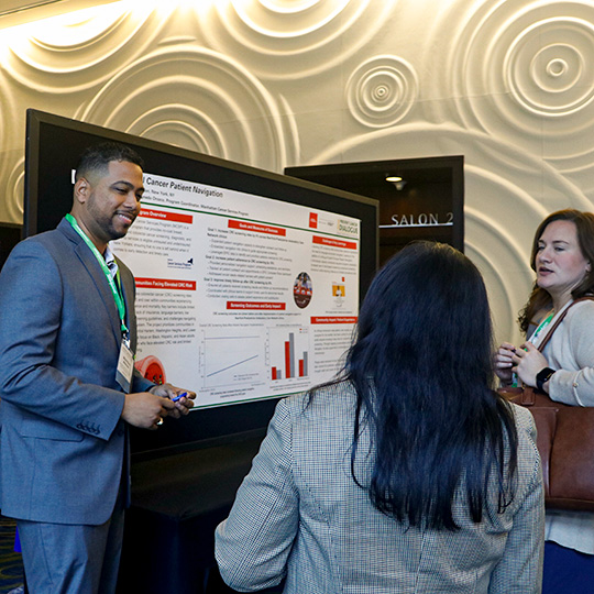 A group of presenters stand at their posters, explaining information.