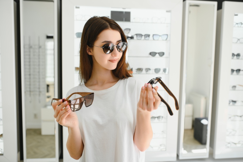 A young woman chooses on sunglasses in an optics store.