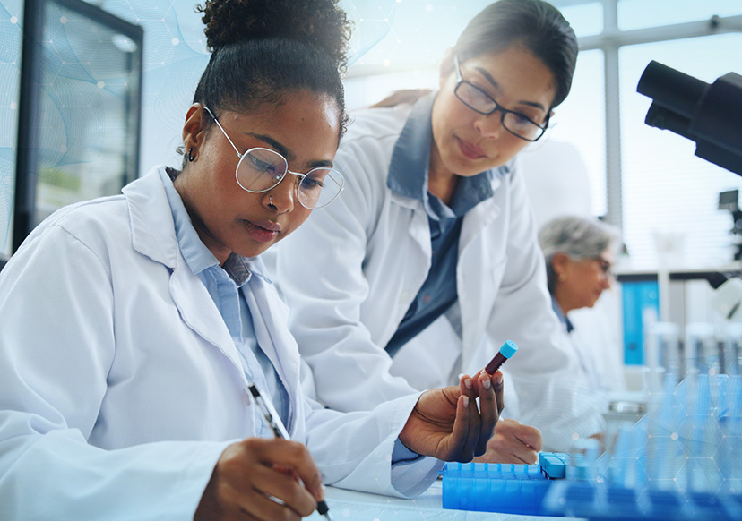 Two young women in white lab coats make observations in a laboratory.