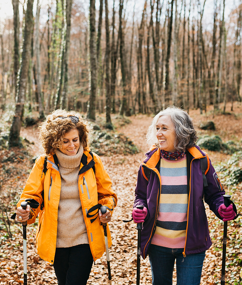 Two women in their 50s enjoying a fall hike in the woods.