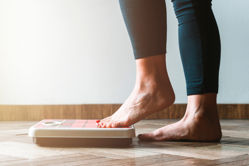 Female checking weight getting on the scale - self care and body positivity concept - warm flare on left
